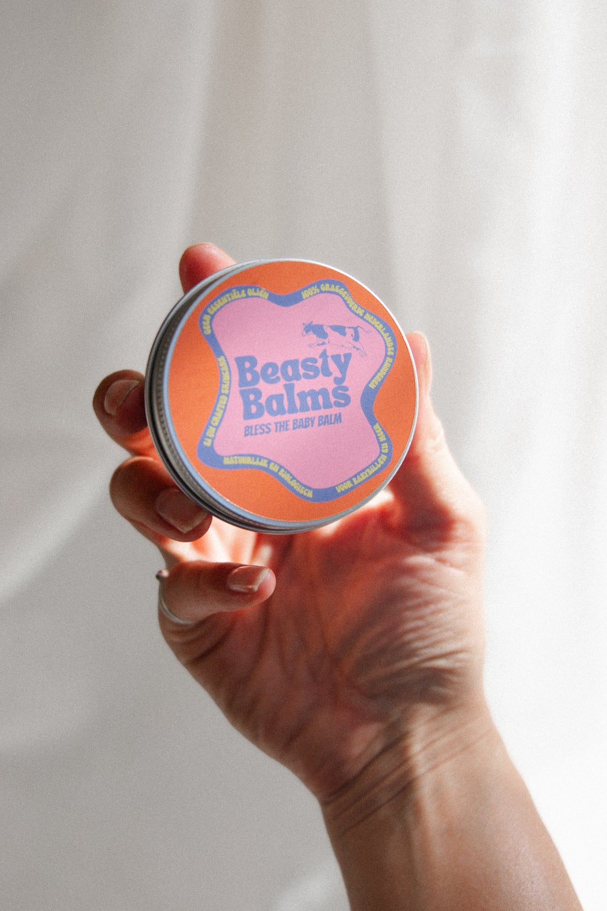 Hand holding a tin of Bless the Baby natural baby balm