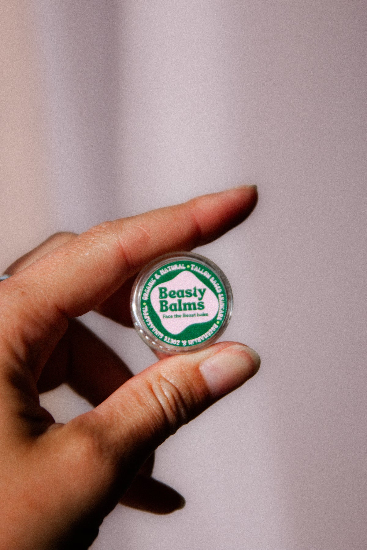 Fingers holding a single Face the Beast tester jar with a green and pink label.
